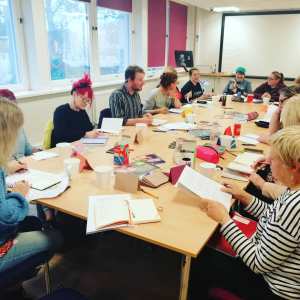14 poets around a table, all writing and giggling.