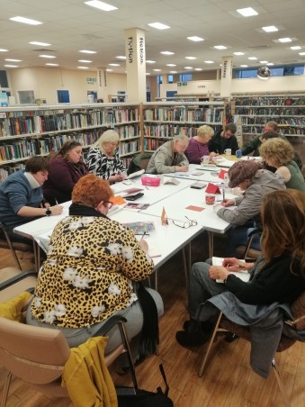 12 people sitting around a table in a library, all writing. So busy we had to pull out the emergency table!