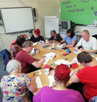 10 poets sitting around tables, all writing.