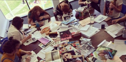 Young people around a table covered in magazines, all writing.