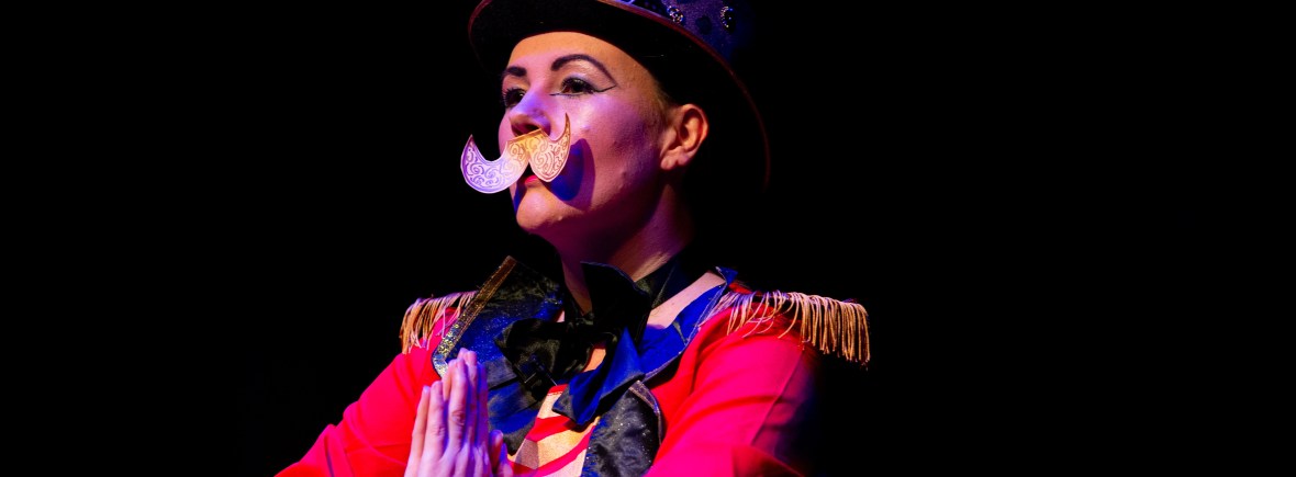 Lisette is wearing ringmistress costume, a top hat and a paper moustache. photo credit -taken at the Disconsortia DIY Cabaret by Kev Howard