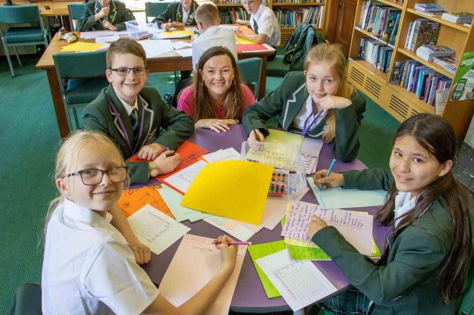 photo of Lisette and 4 children, all smiling at the camera, with loads of work and pens on their circular table
