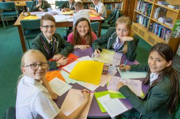 photo of Lisette and 4 children, all smiling at the camera, with loads of work and pens on their circular table